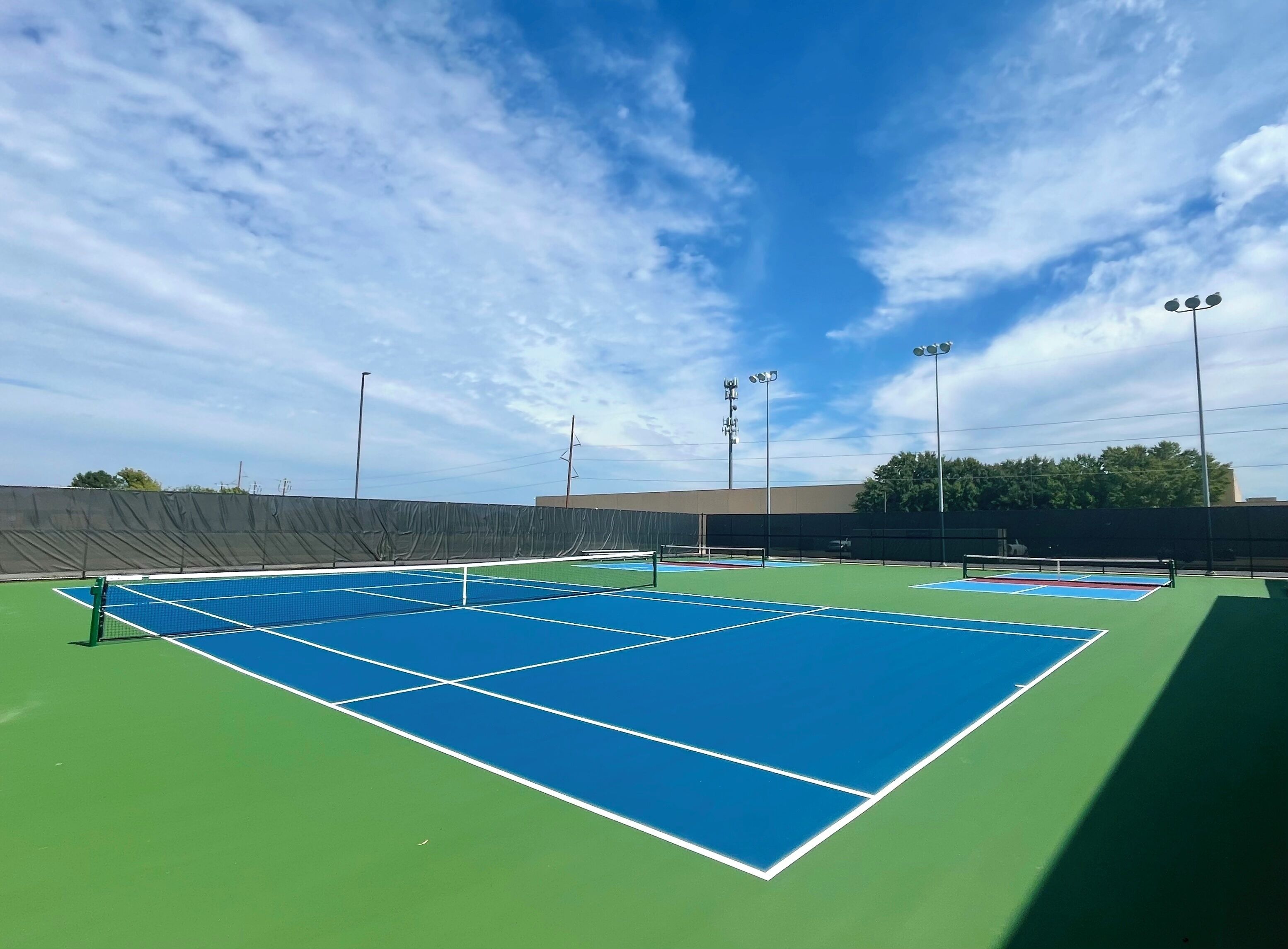 A tennis court with multiple courts, surrounded by a fence, under a clear sky.