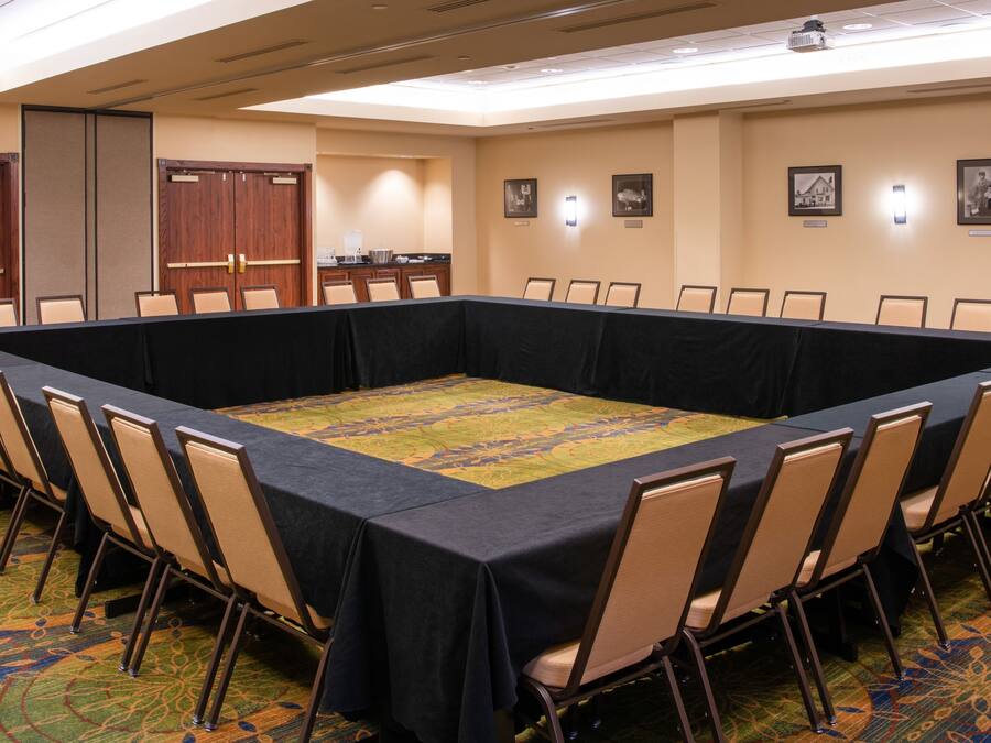A conference room with a long table surrounded by chairs, a kitchenette, and a door.