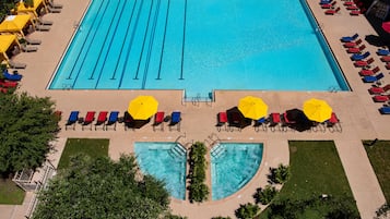 Uma grande piscina retangular com várias pistas de natação, rodeada por espreguiçadeiras e guarda-sóis, e uma área de piscina menor com borda curva.