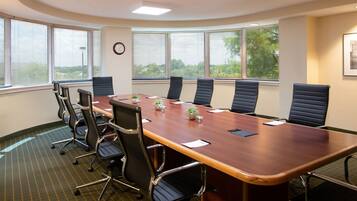 Sala de conferência com uma mesa comprida, seis cadeiras e janelas amplas com persianas.