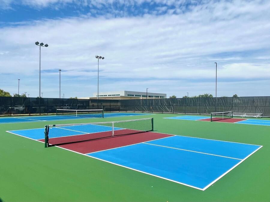 En utomhusbana för tennis med flera banor, ett nät och ett staket runt omkring.