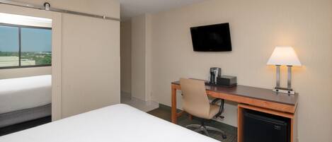 Una habitación de hotel con cama, escritorio con silla, televisor, cafetera y lámpara.