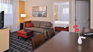 Habitación de hotel con sofá, una mesita, televisión y escritorio con lámpara.