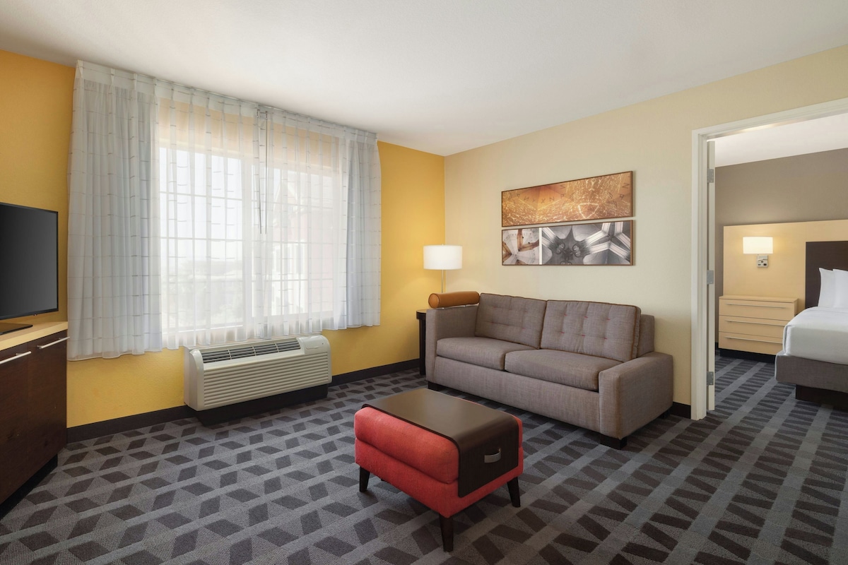 A hotel room with a sofa, a small table, a television, a heater, and a window with curtains.
