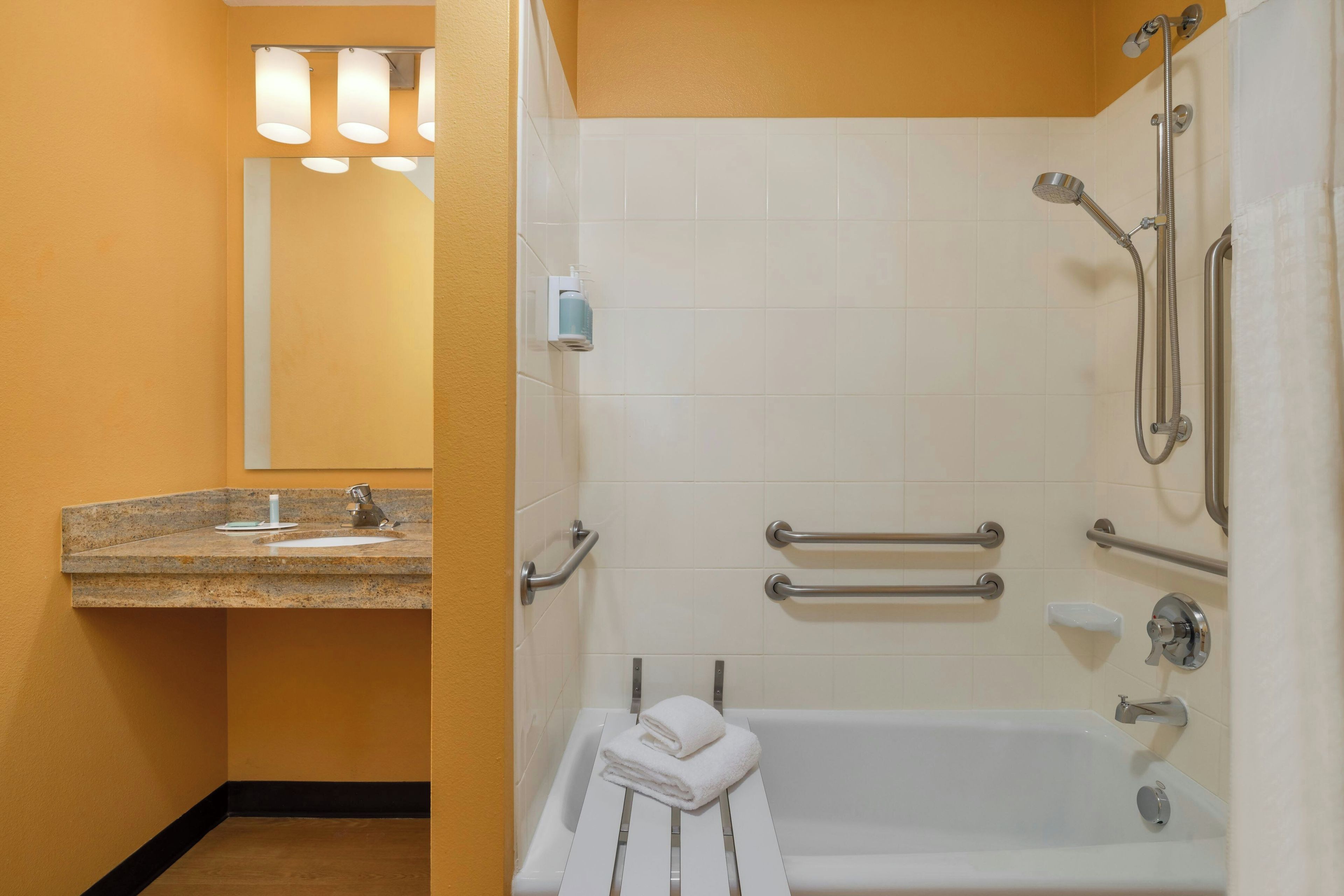 A bathroom with a bathtub, a sink, a mirror, and a shower with grab bars.