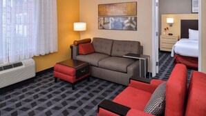 Habitación de hotel con sofá, un sillón rojo, una mesita, una lámpara y una cama.