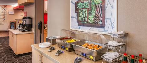 A buffet setup with various food items, a coffee machine, and condiments.