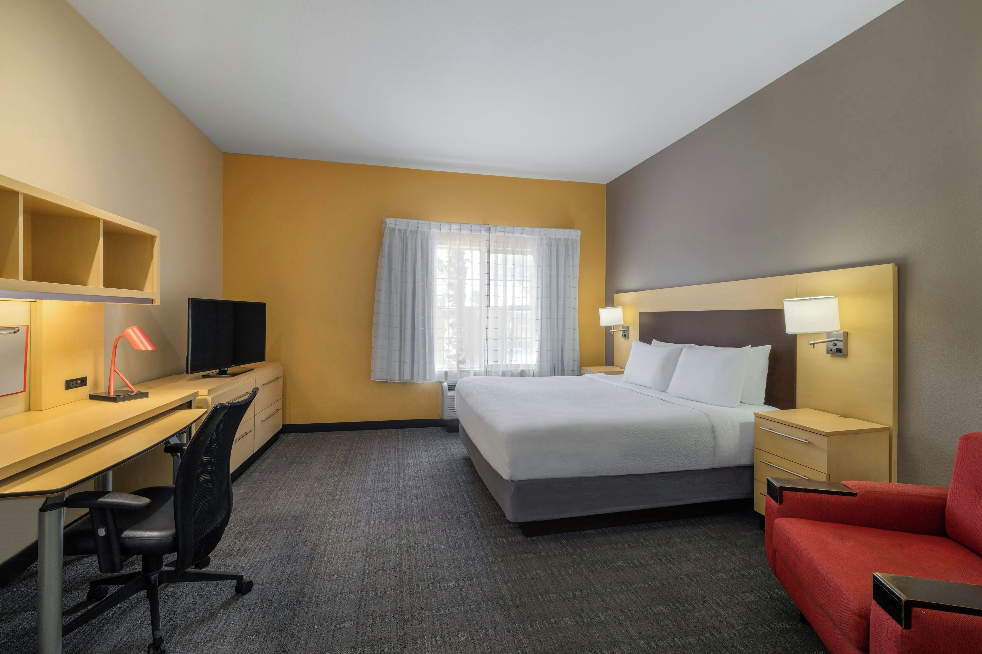 A hotel room with a bed, desk, chair, TV, and a red sofa.