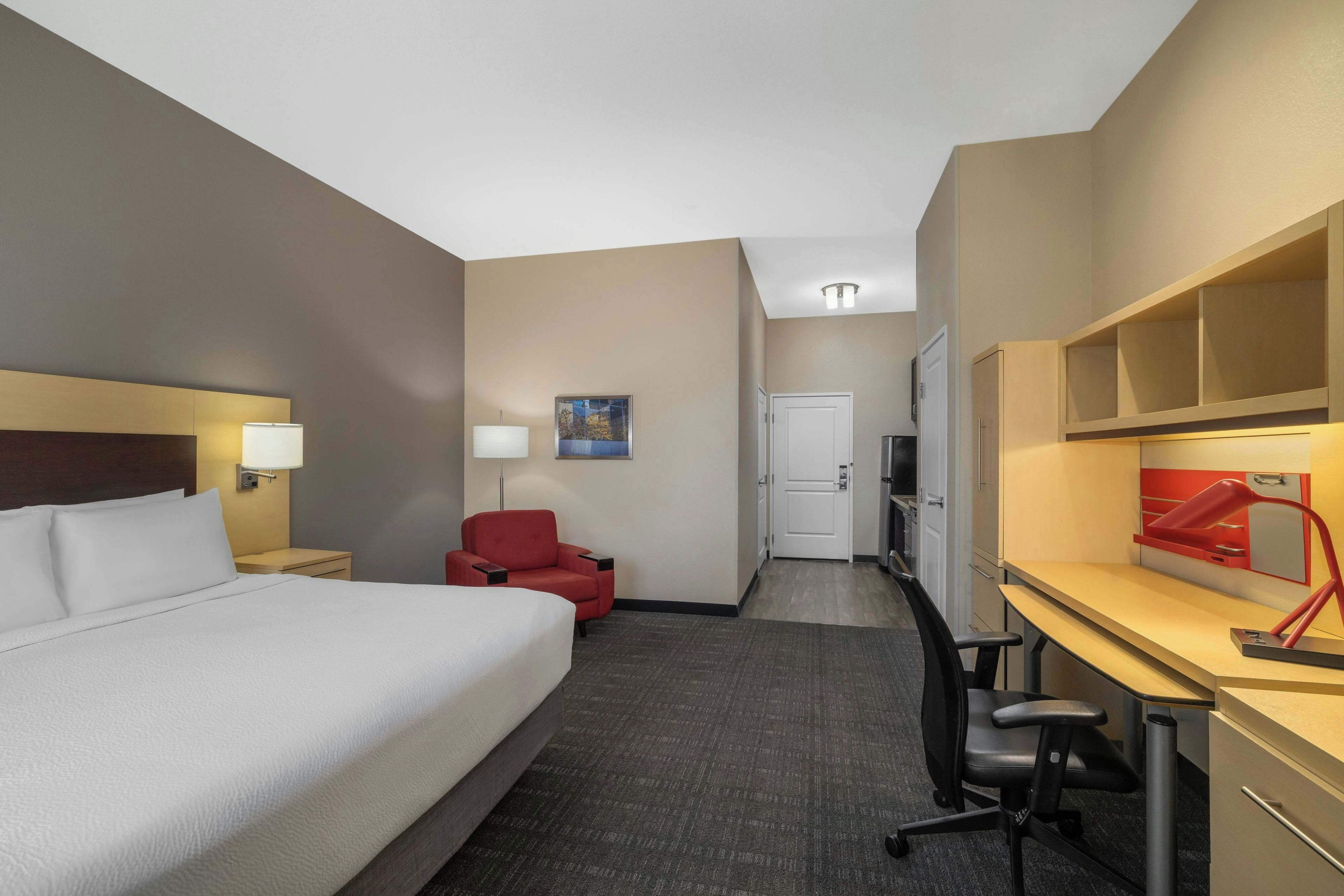 Une chambre d’hôtel avec un lit, un bureau, une chaise et un fauteuil rouge.