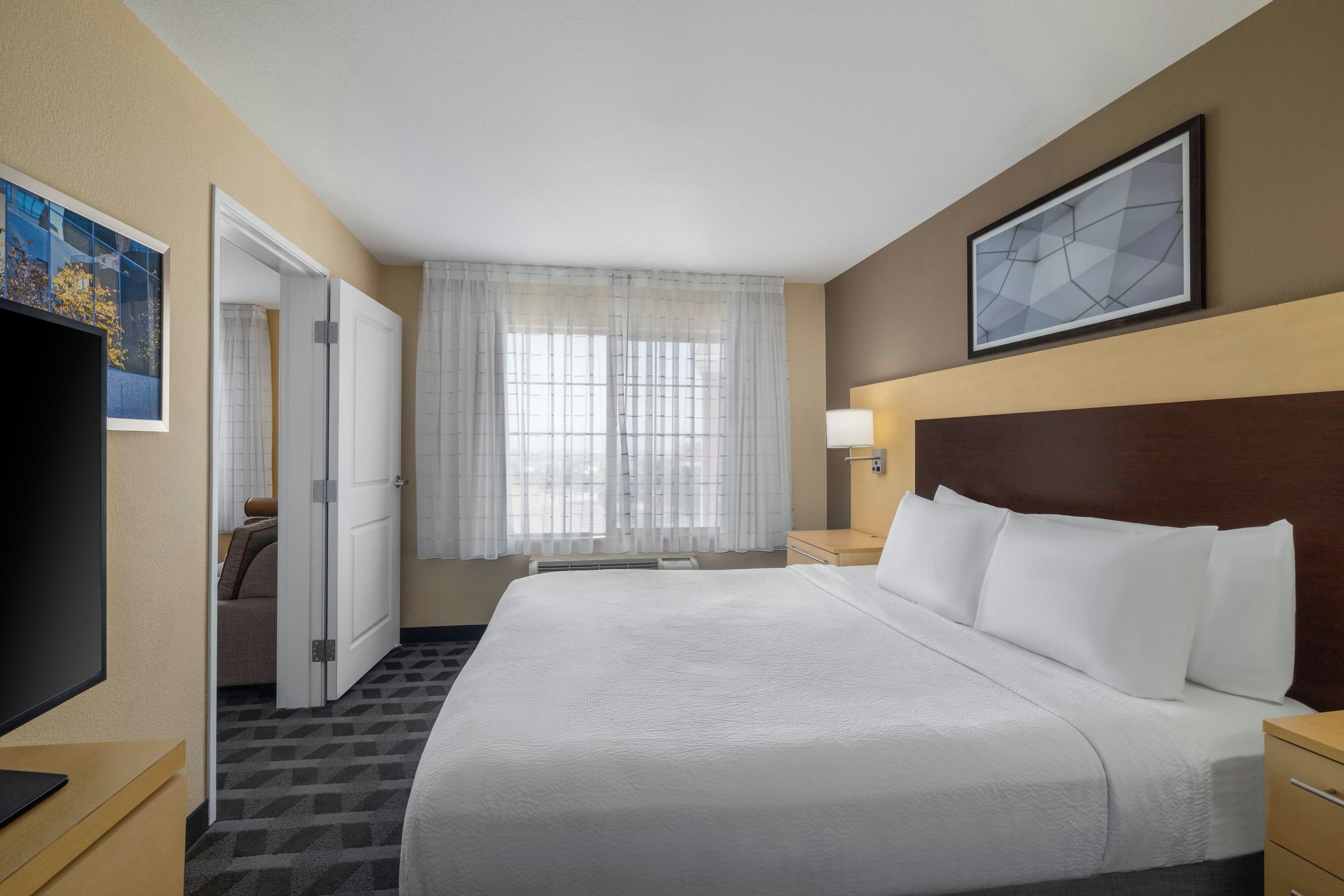 Habitación de hotel con una cama grande, un televisor de pantalla plana, un escritorio y una ventana con cortinas translúcidas.