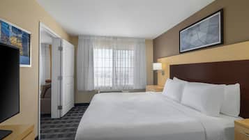 Habitación de hotel con una cama grande, un televisor de pantalla plana, un escritorio y una ventana con cortinas translúcidas.
