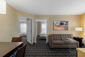 A hotel room with a sofa, a dining table, a lamp, and a painting on the wall.