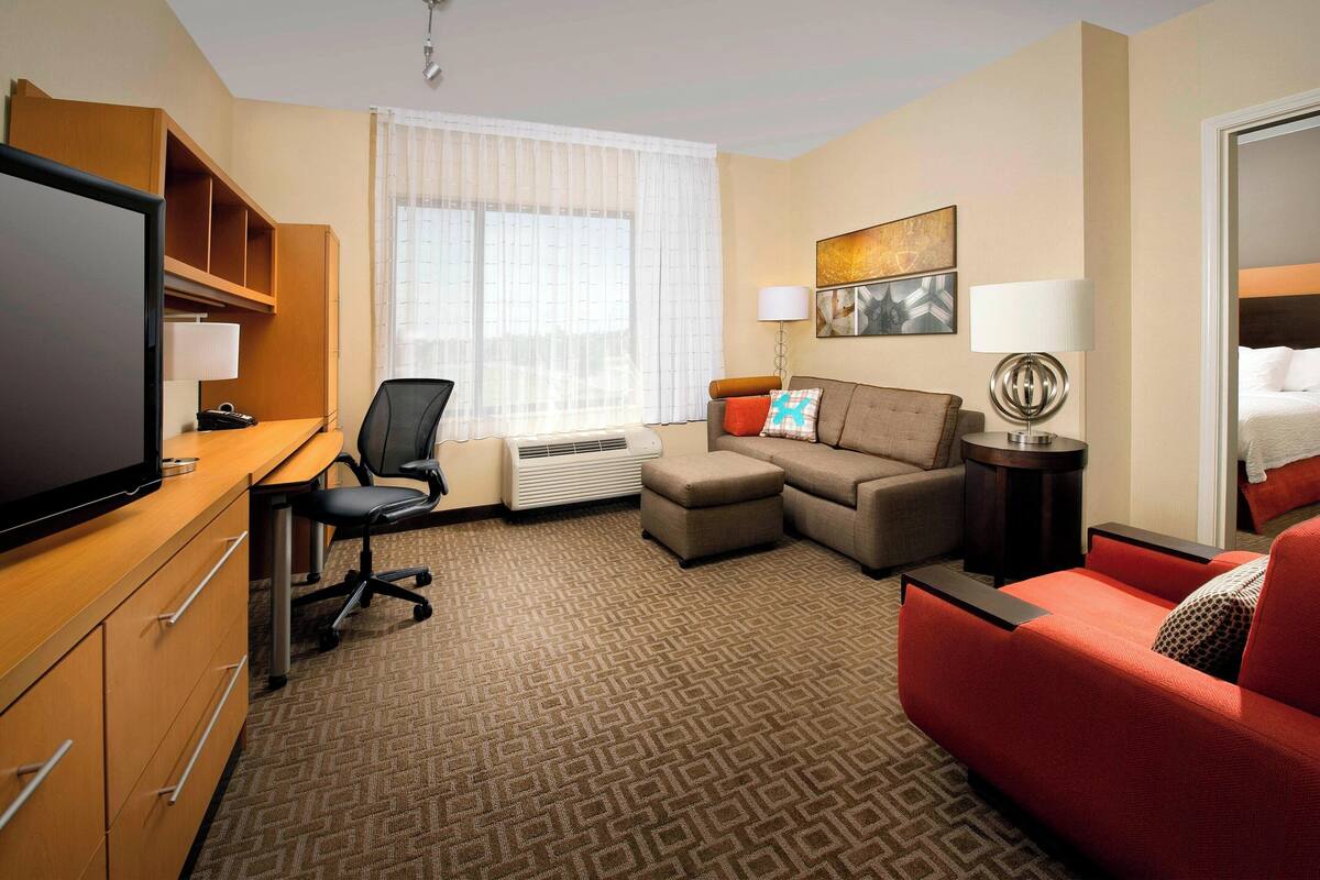 A hotel room with a desk, chair, sofa, and a television.