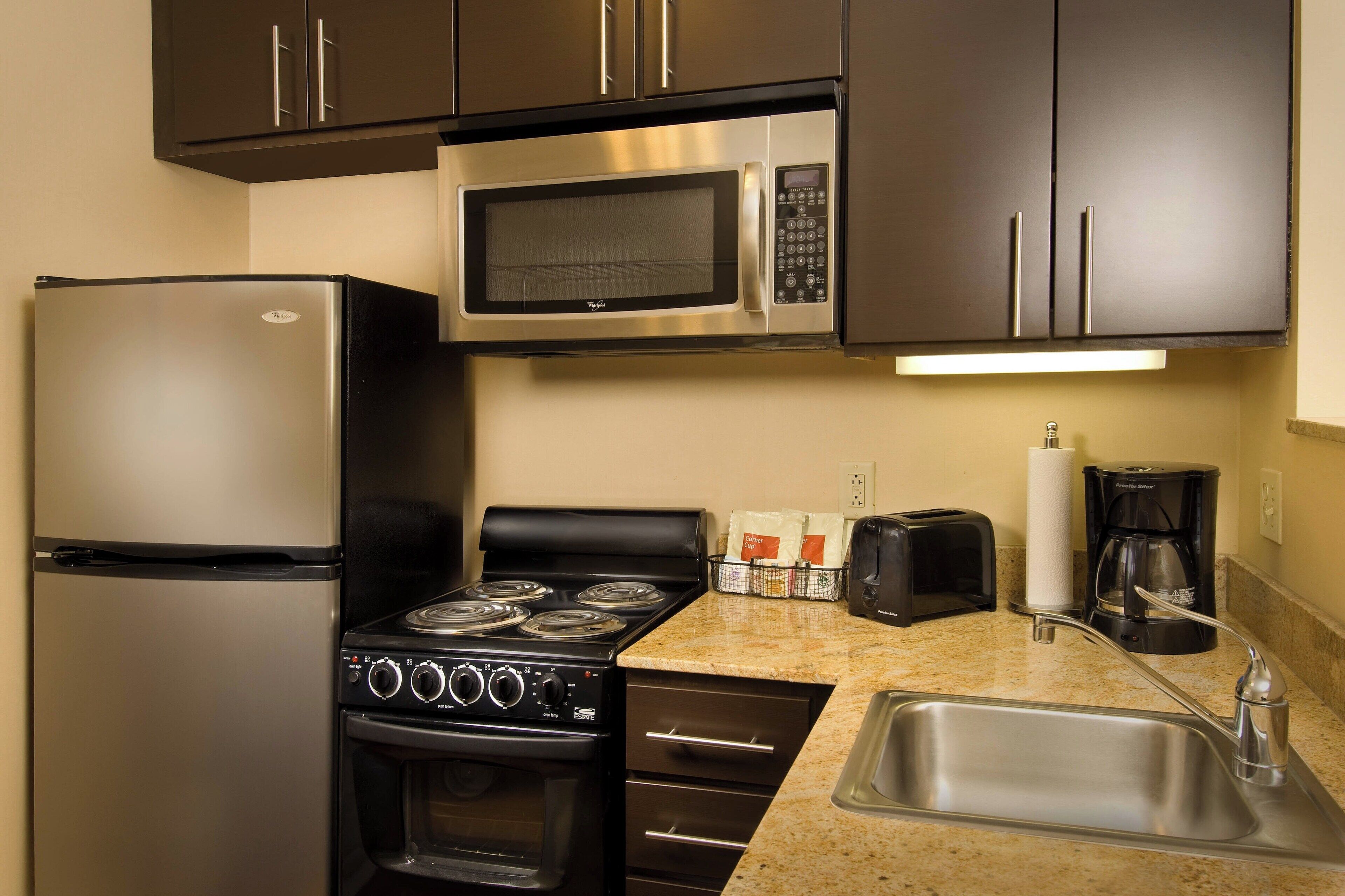 Una cocina compacta equipada con refrigerador, microondas, estufa, horno y pileta.