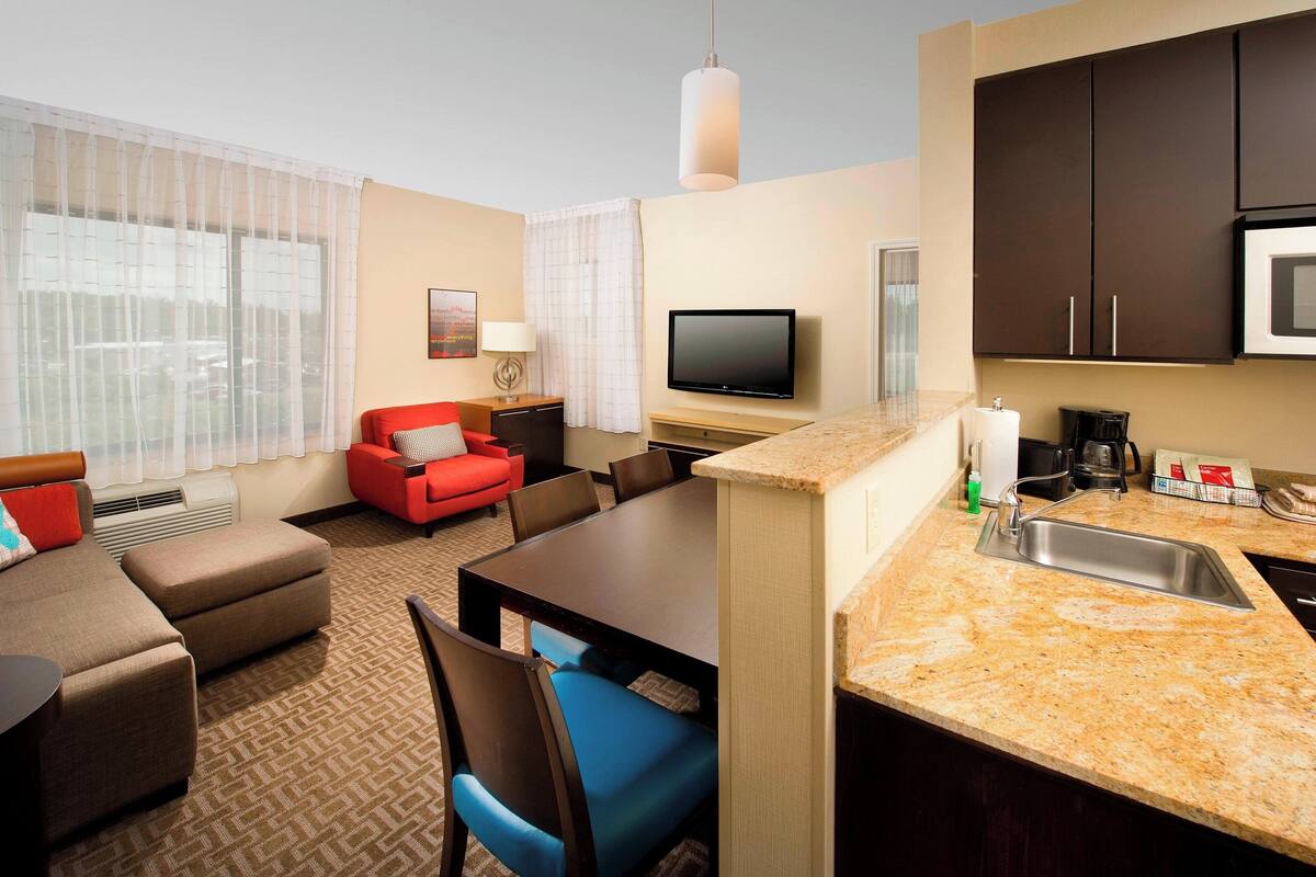 A hotel room with a living area, dining table, kitchenette, and a TV.