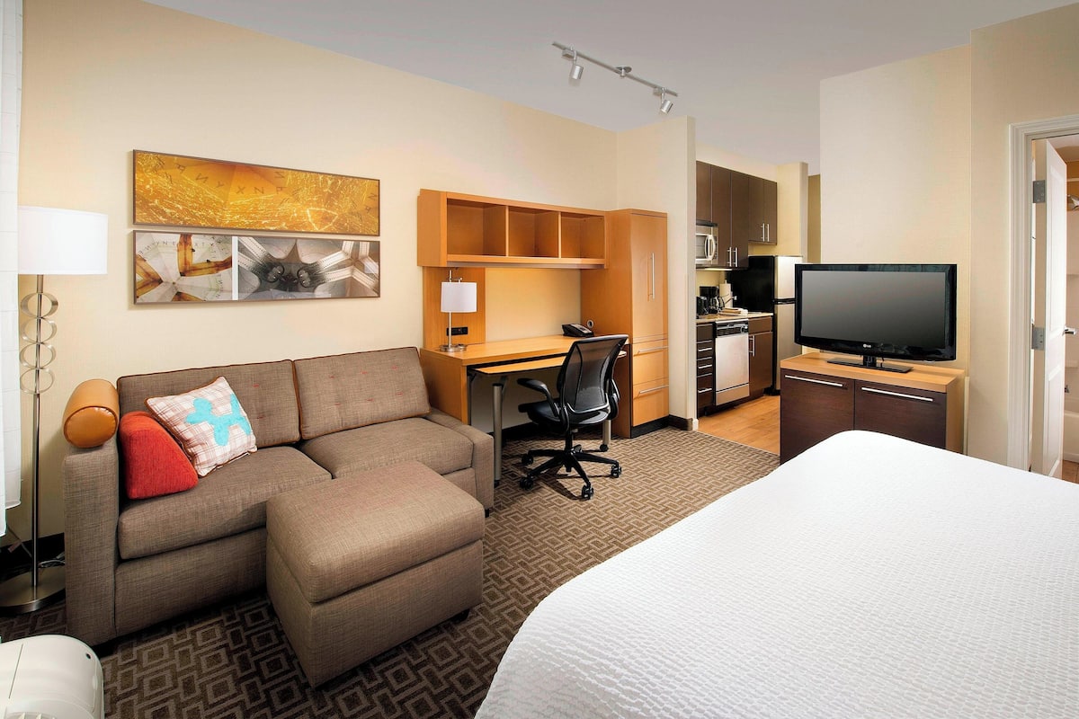 A hotel room with a bed, a sofa, a desk, a chair, a television, and a kitchenette.