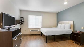 A modern hotel room with a bed, a TV on a dresser, a heater, and a window with blinds.