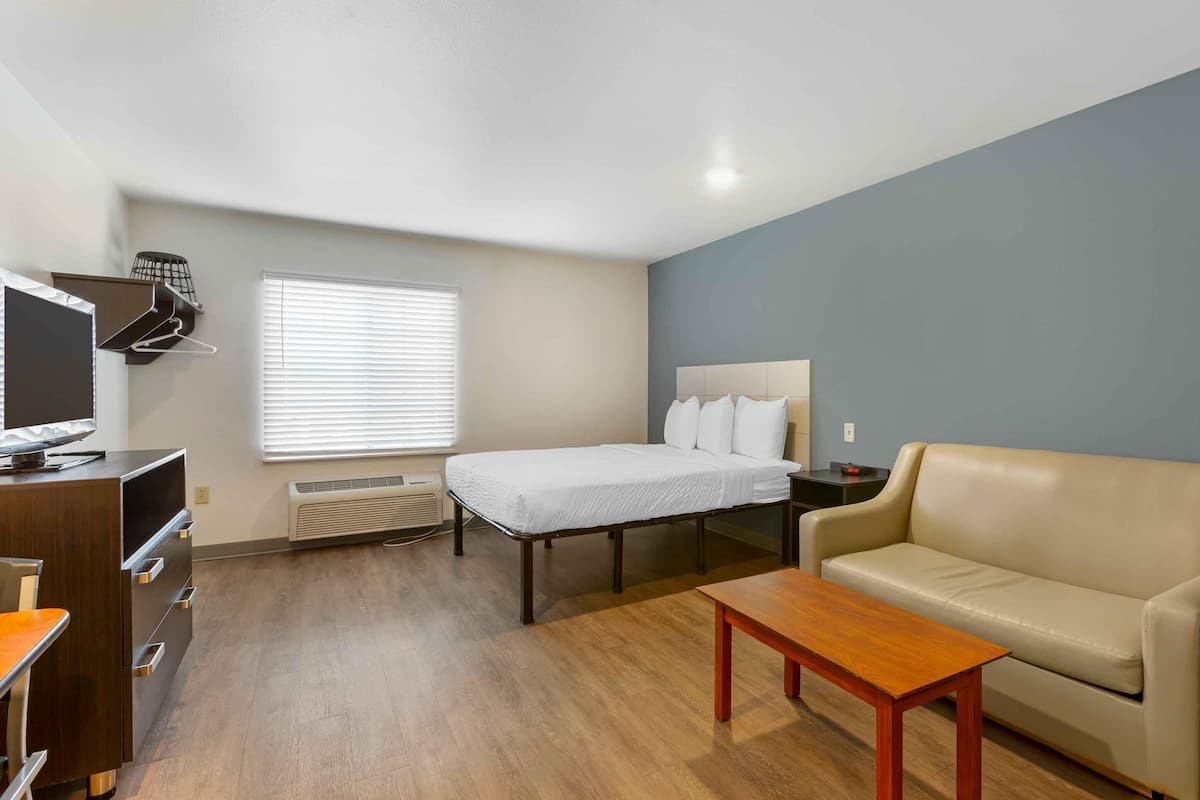 A compact hotel room with a bed, a sofa, a TV, and a desk.