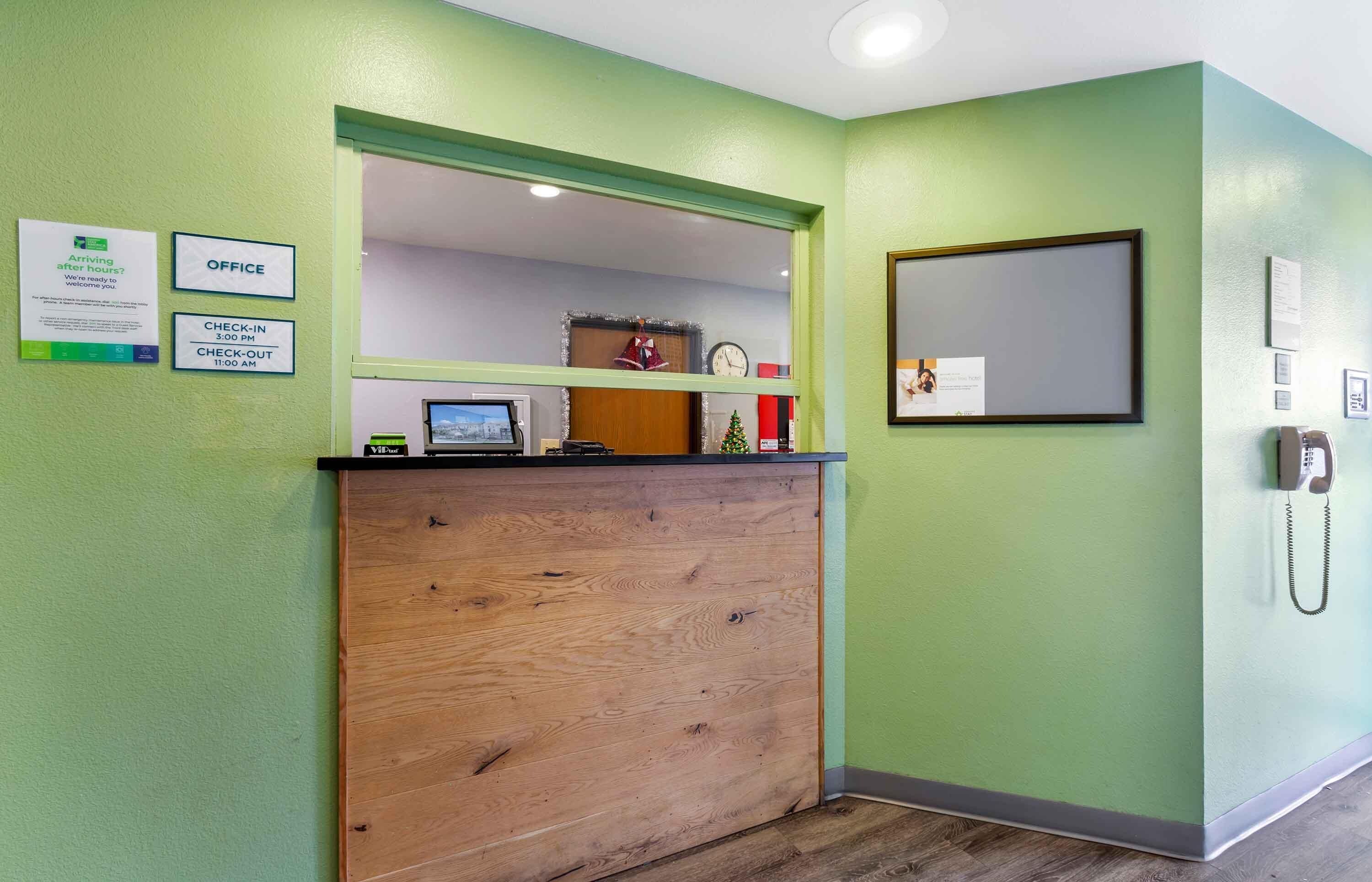 Ein Empfangsschalter mit Holzbeschichtung, eine Schilder für Check-in/Check-out, ein gerahmtes Bild und ein Telefon an der Wand.