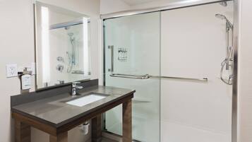 Un baño moderno con ducha de vidrio, tocador de madera con lavabo y un espejo grande.