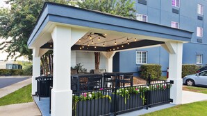 A covered outdoor seating area with tables and chairs, a black metal fence, and string lights.