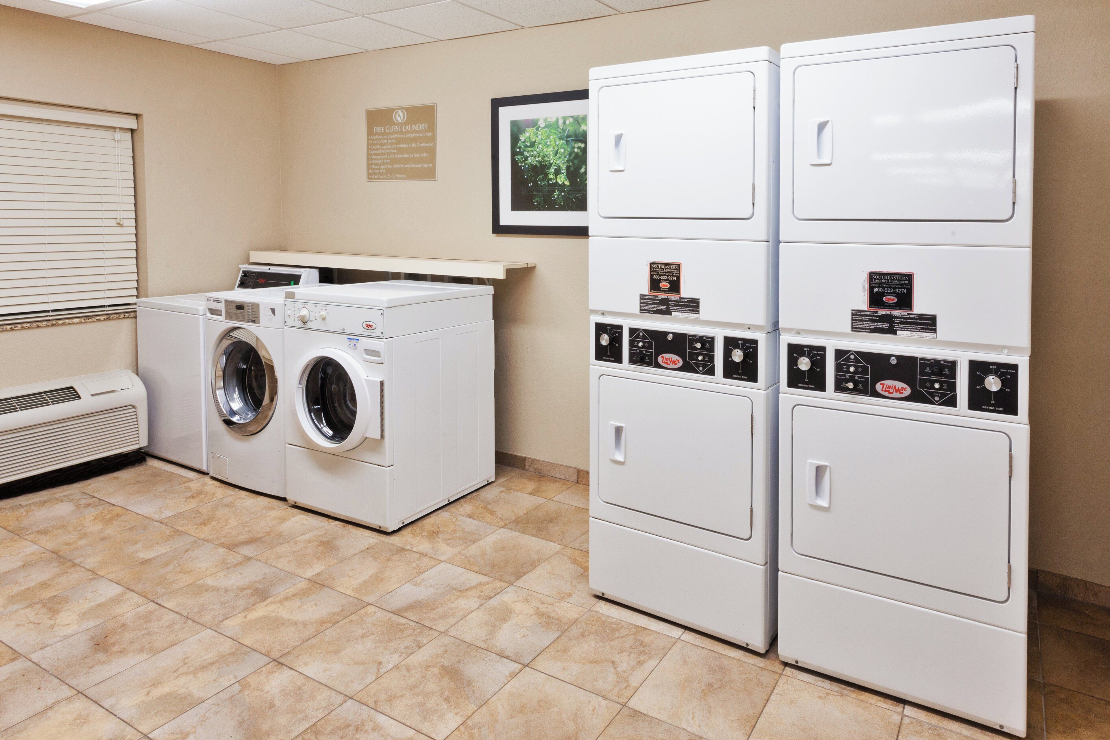 A laundry facility with a front-loading washer and dryer, a wall-mounted control panel, and a framed picture.