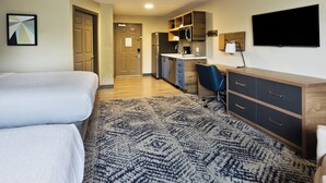 A hotel room with a bed, a desk, a kitchenette, and a TV.