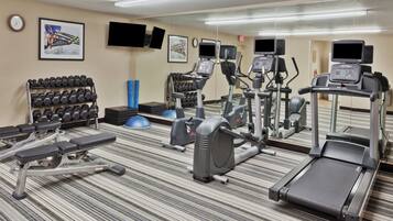 Un gimnasio de hotel con cintas de correr, elípticas, una prensa de banca y un estante con mancuernas.