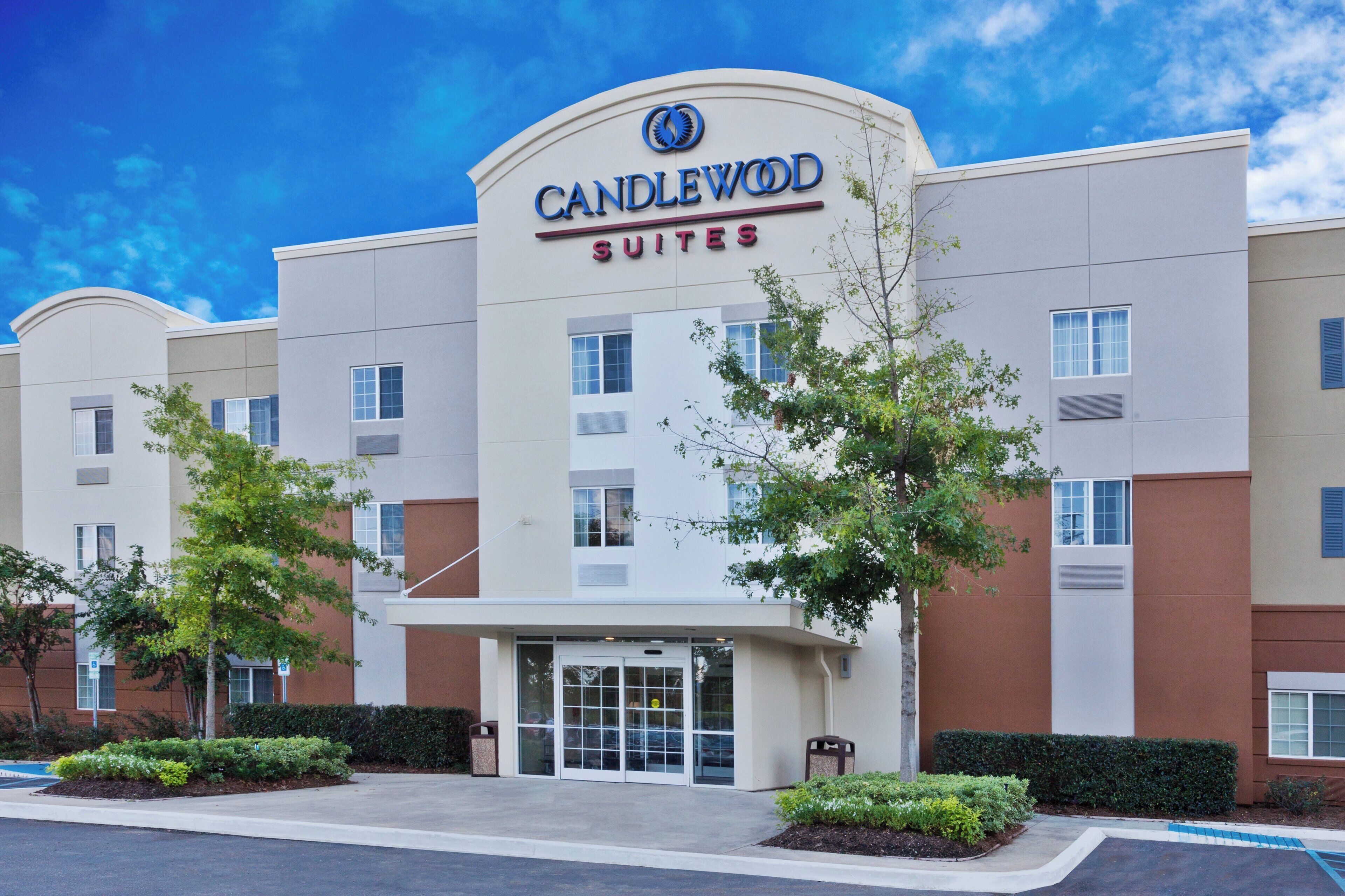 Hotellin julkisivu on moderni, siinä on selkeästi näkyvä «CANDLEWOOD SUITES» -kyltti, ja sisäänkäynti on portilla varustettu.