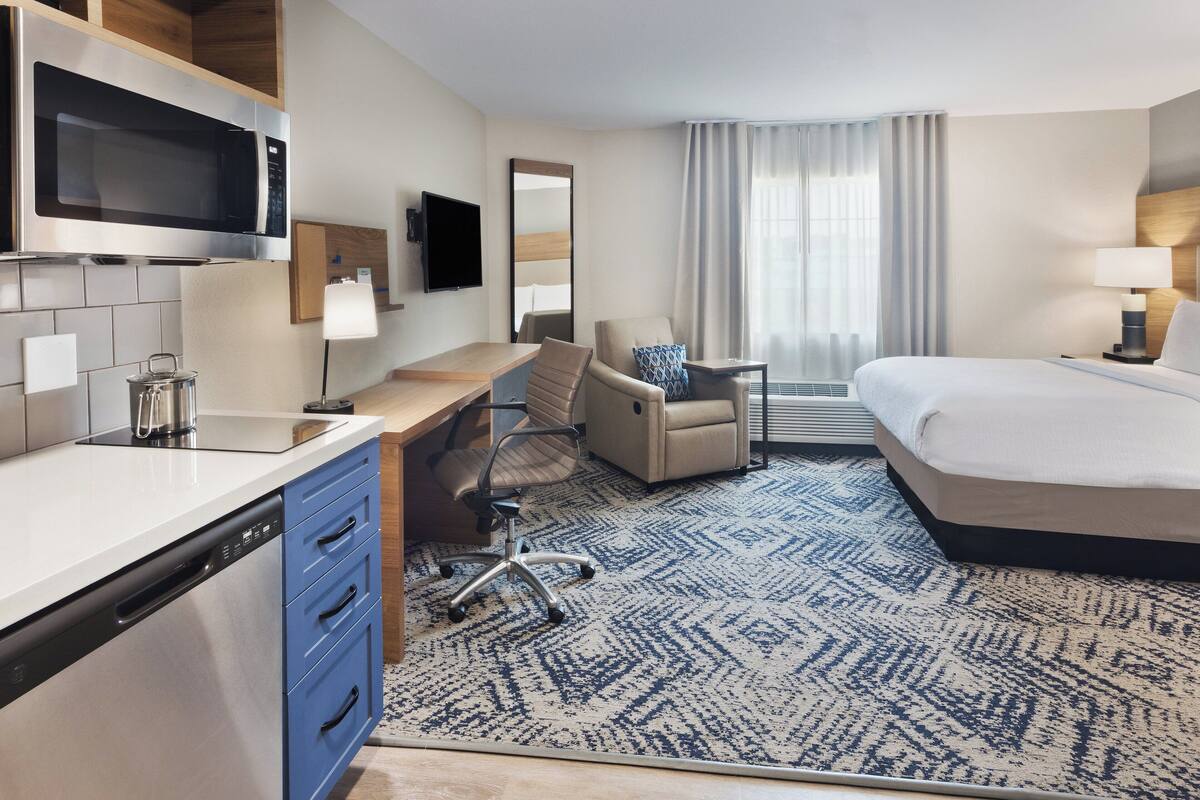Une chambre d’hôtel comprenant un lit, un bureau avec une chaise, un four à micro-ondes, une télévision et une grande fenêtre avec des rideaux.