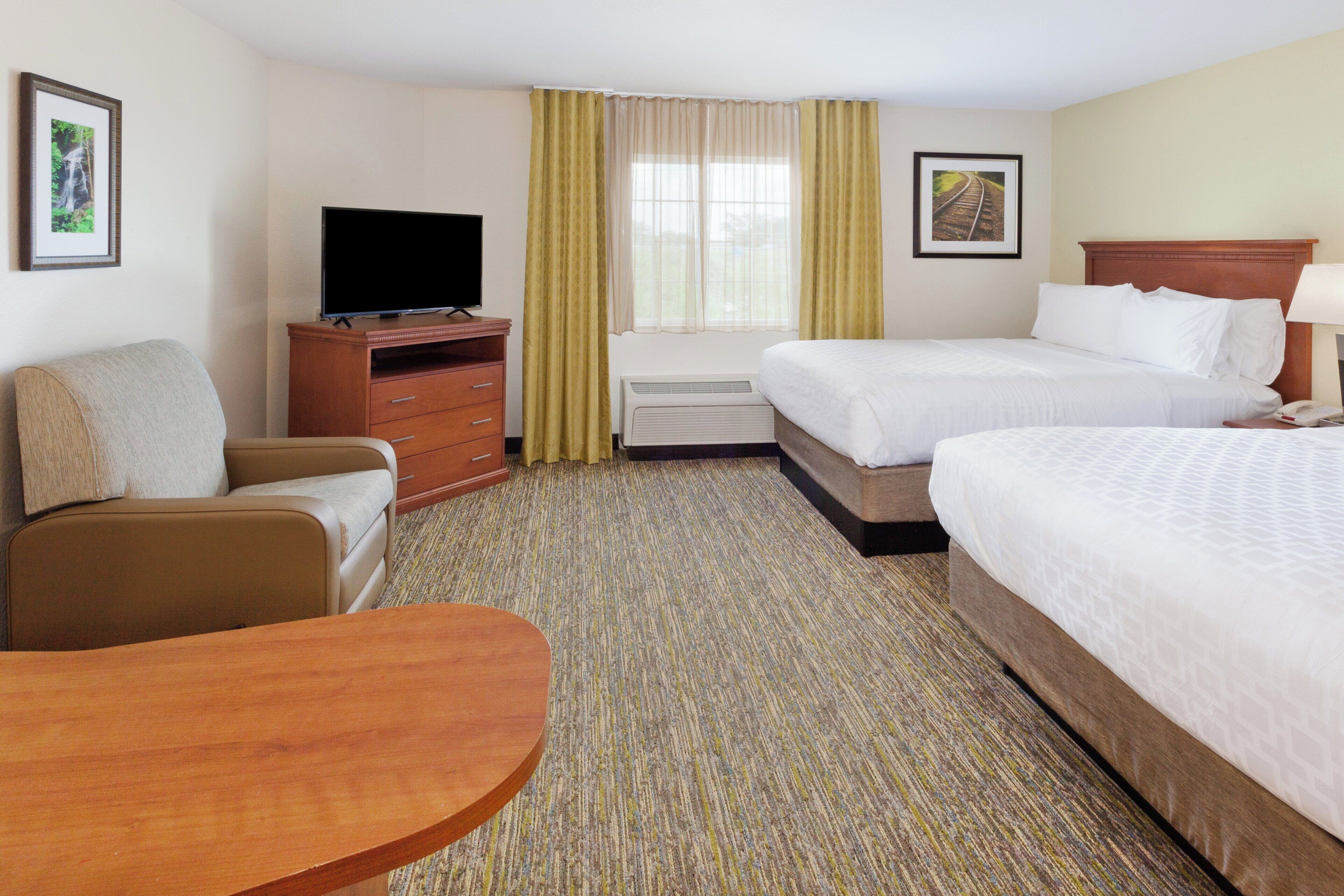 A hotel room with two beds, a TV, a desk, and a chair.