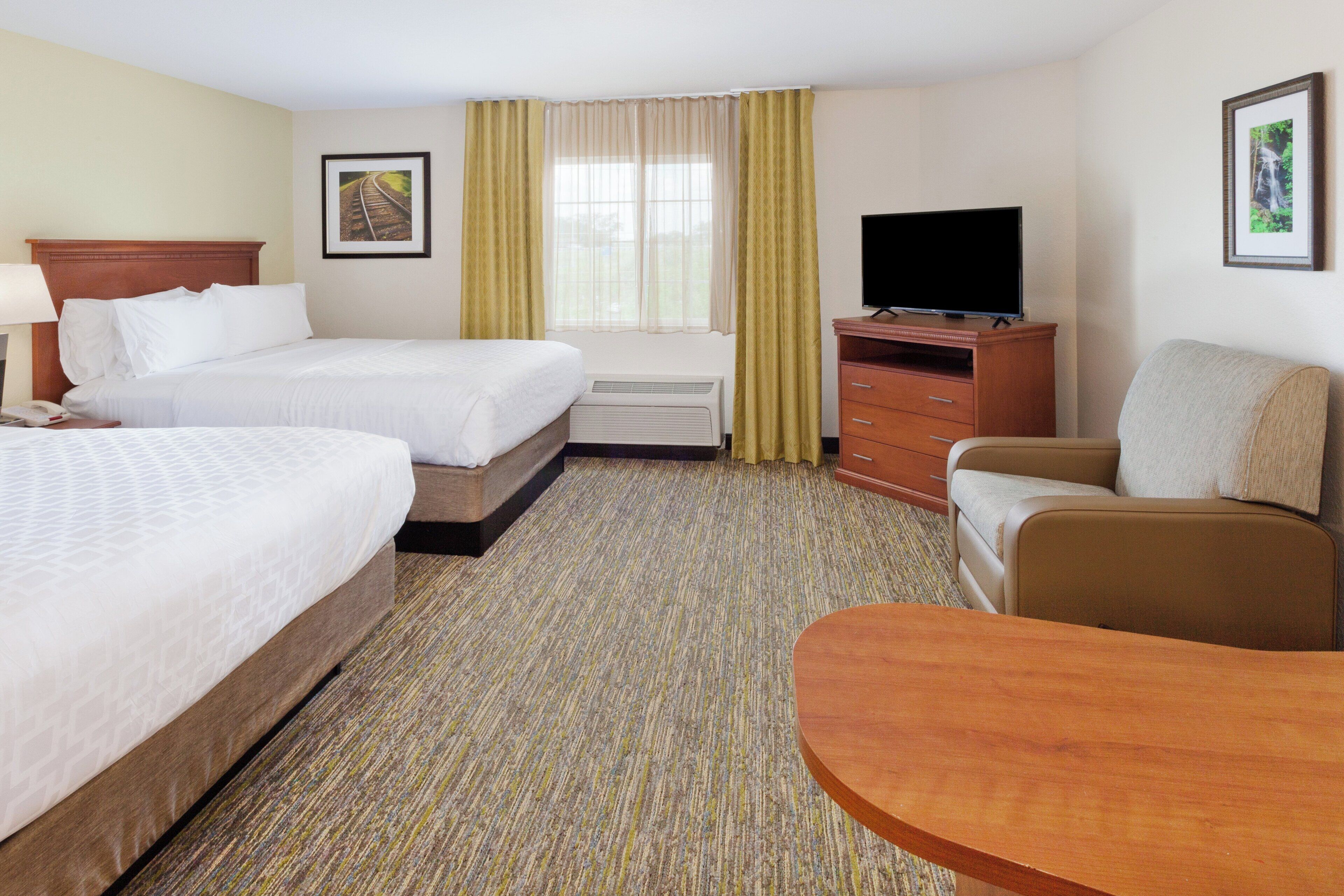 A hotel room with two beds, a television, a desk, and a chair.