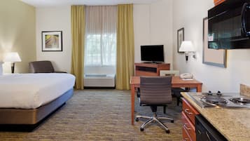 Habitación de hotel con cama, escritorio, silla, televisión y kitchenette.