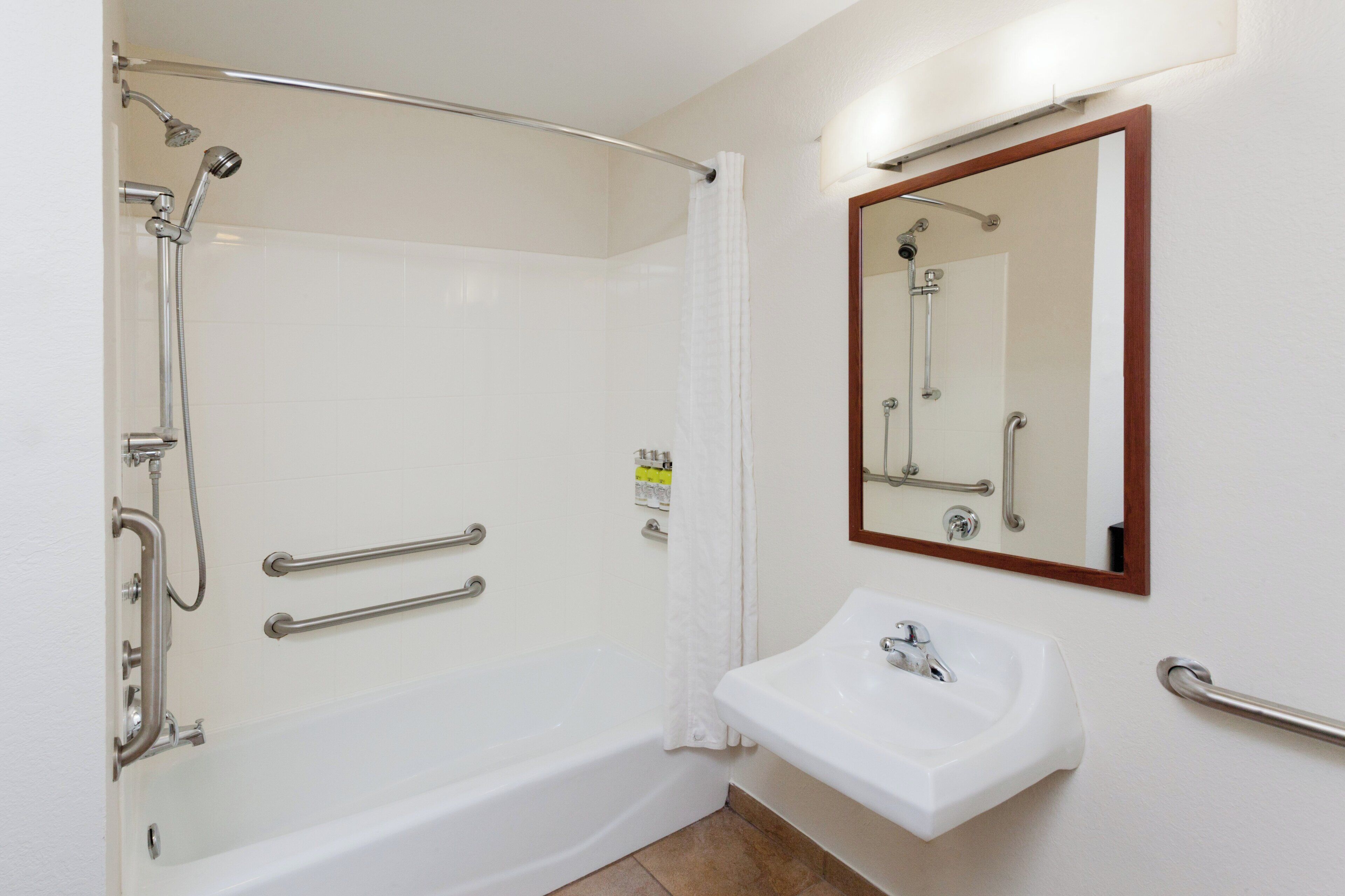 A bathroom with a walk-in shower, grab bars, a sink, and a mirror.