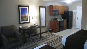 Quarto de hotel com cama, escrivaninha, cadeira, cozinha compacta e um quadro na parede.