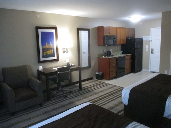 A hotel room with a bed, a desk, a chair, a kitchenette, and a framed picture on the wall. - Best Western Plus Crawfordsville Hotel (Crawfordsville)