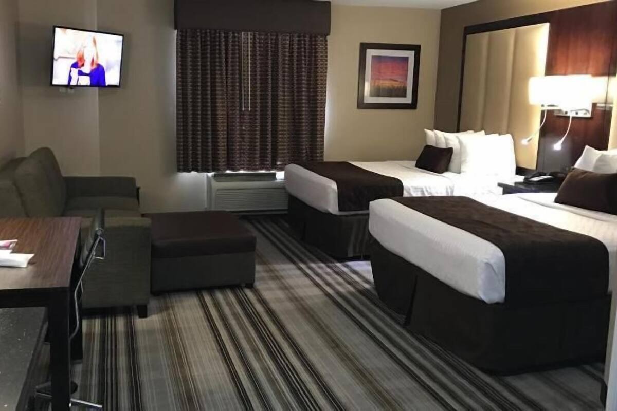 A hotel room with two beds, a desk, a chair, a TV, and a window with curtains.