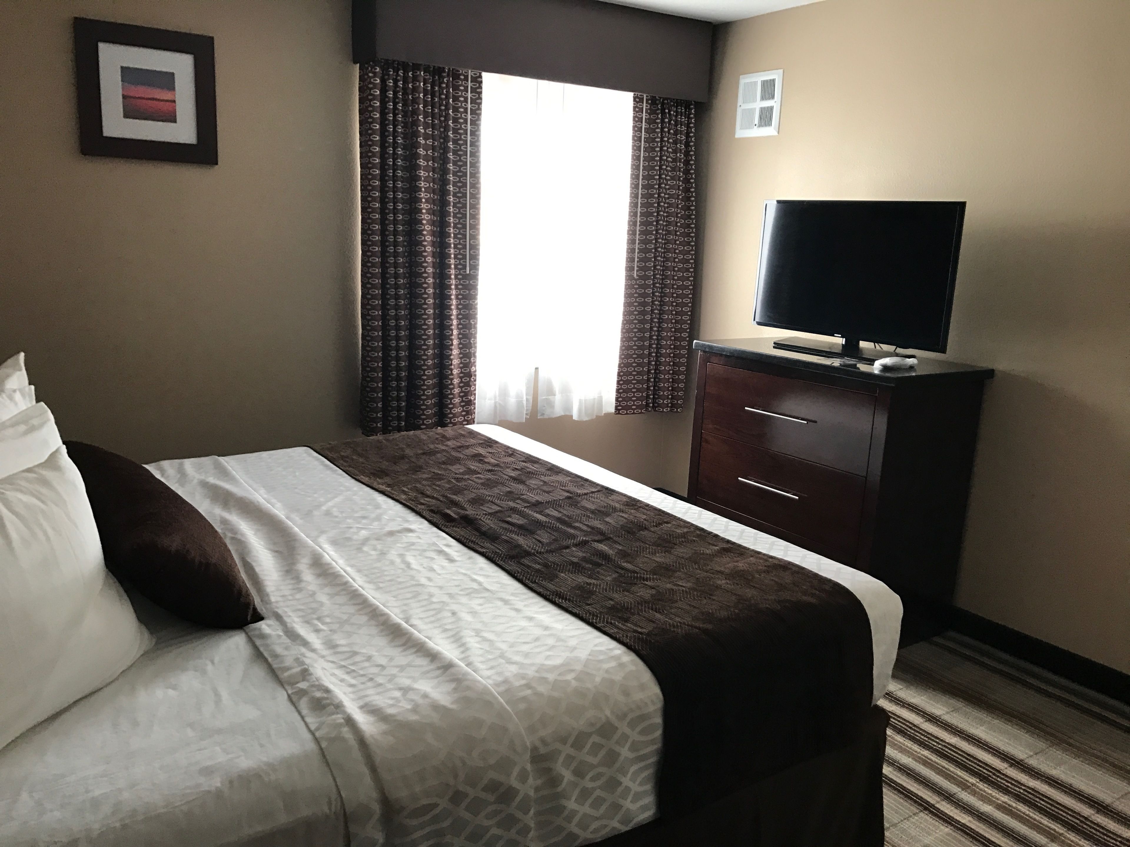 Une chambre d’hôtel avec un lit, un téléviseur posé sur une commode et une fenêtre avec des rideaux.
