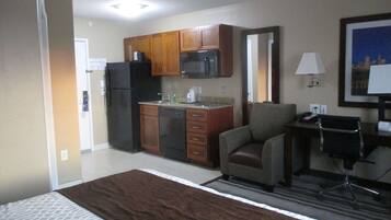 Una habitación de hotel con cama, kitchenette, una silla, escritorio y lámpara.