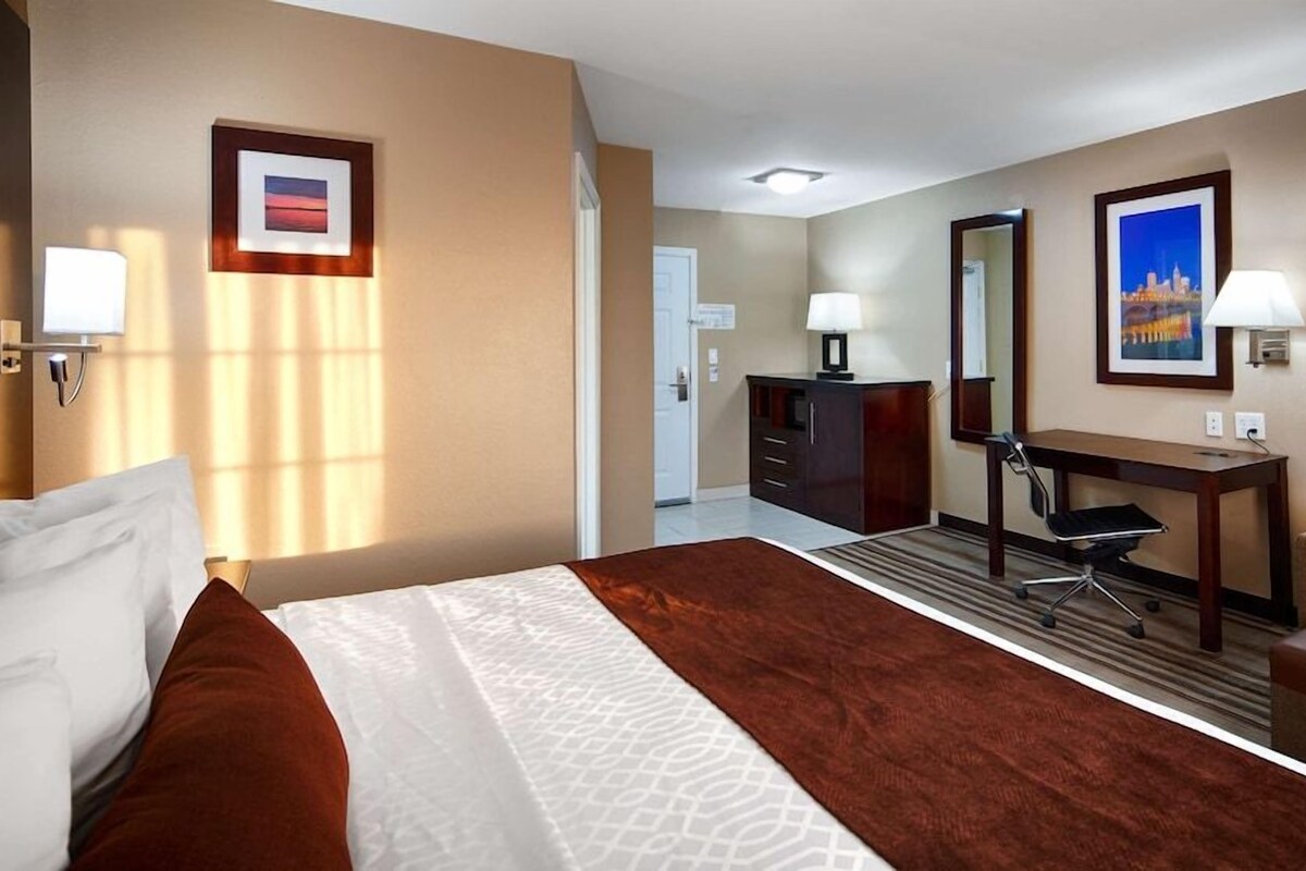 Een hotelkamer met een bed, een bureau, een stoel, een dressoir en twee foto's in lijsten aan de muur.