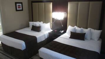 Quarto de hotel com duas camas de solteiro, mesa de cabeceira, abajur e um quadro na parede.