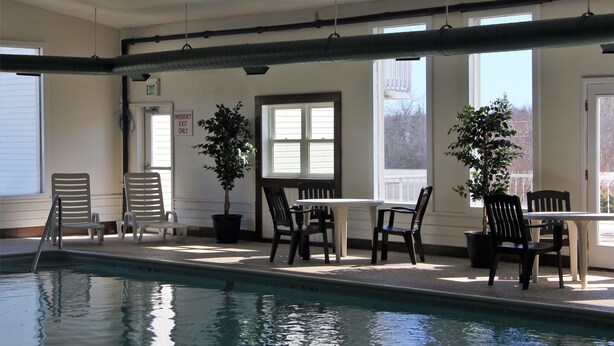 A pool area with a table and chairs, a potted plant, and an emergency exit sign. - Up North Hotel (formerly Voyager Inn) (St Ignace)