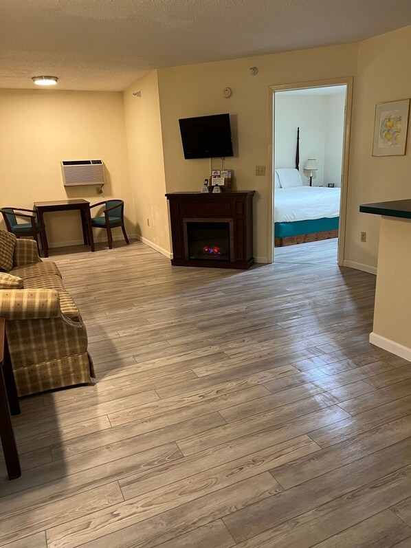 A living room with a fireplace, a television, and a bed in the background. - Up North Hotel (formerly Voyager Inn) (St Ignace)