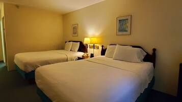 A hotel room with two beds, a bedside table with a lamp, and a painting on the wall.