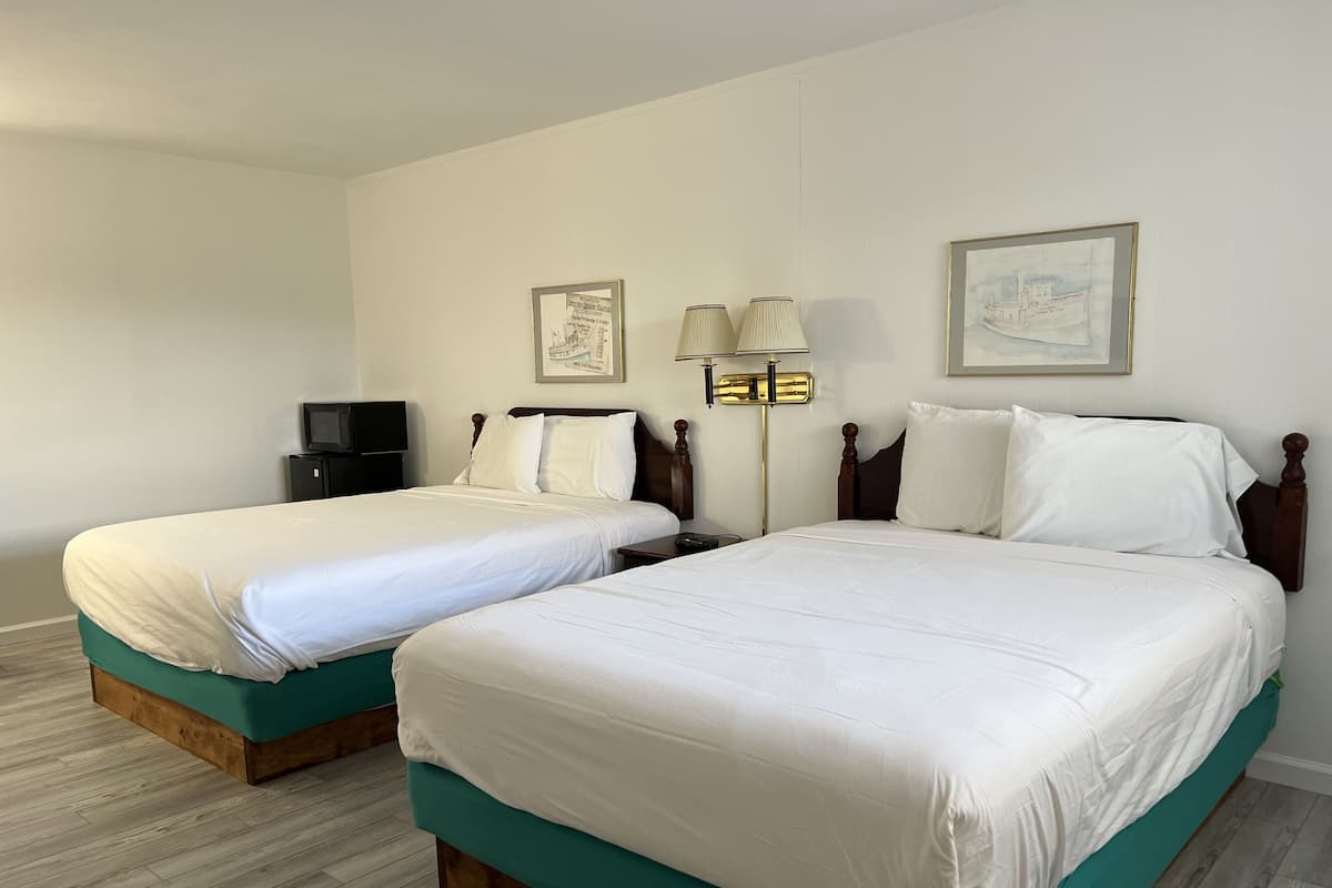 Ett hotellrum med två sängar, en tv, en lampa och inramade konstverk på väggen.
