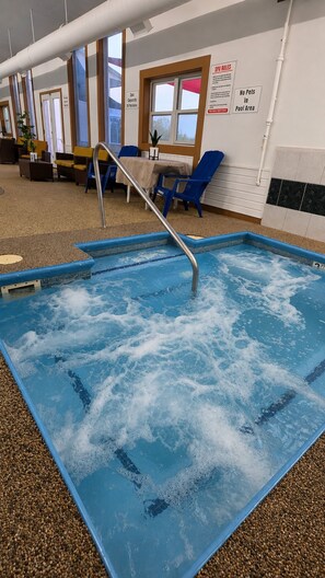 Una piscina tipo spa con una escalera metálica, sillas azules y un cartel que indica que no se permiten mascotas en la zona de la piscina.