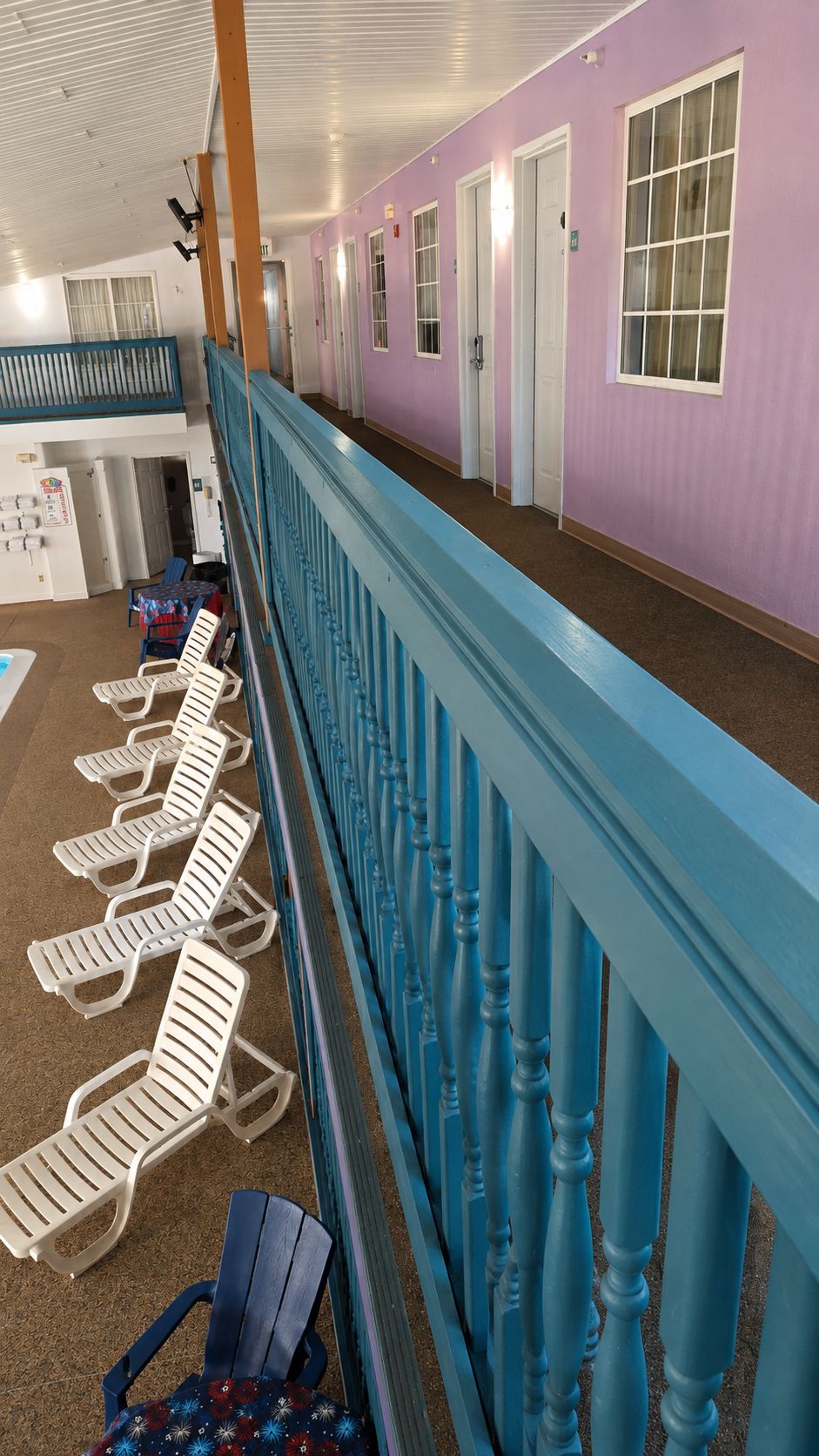 A corridor with a blue railing, white lounge chairs, and doors leading to rooms.