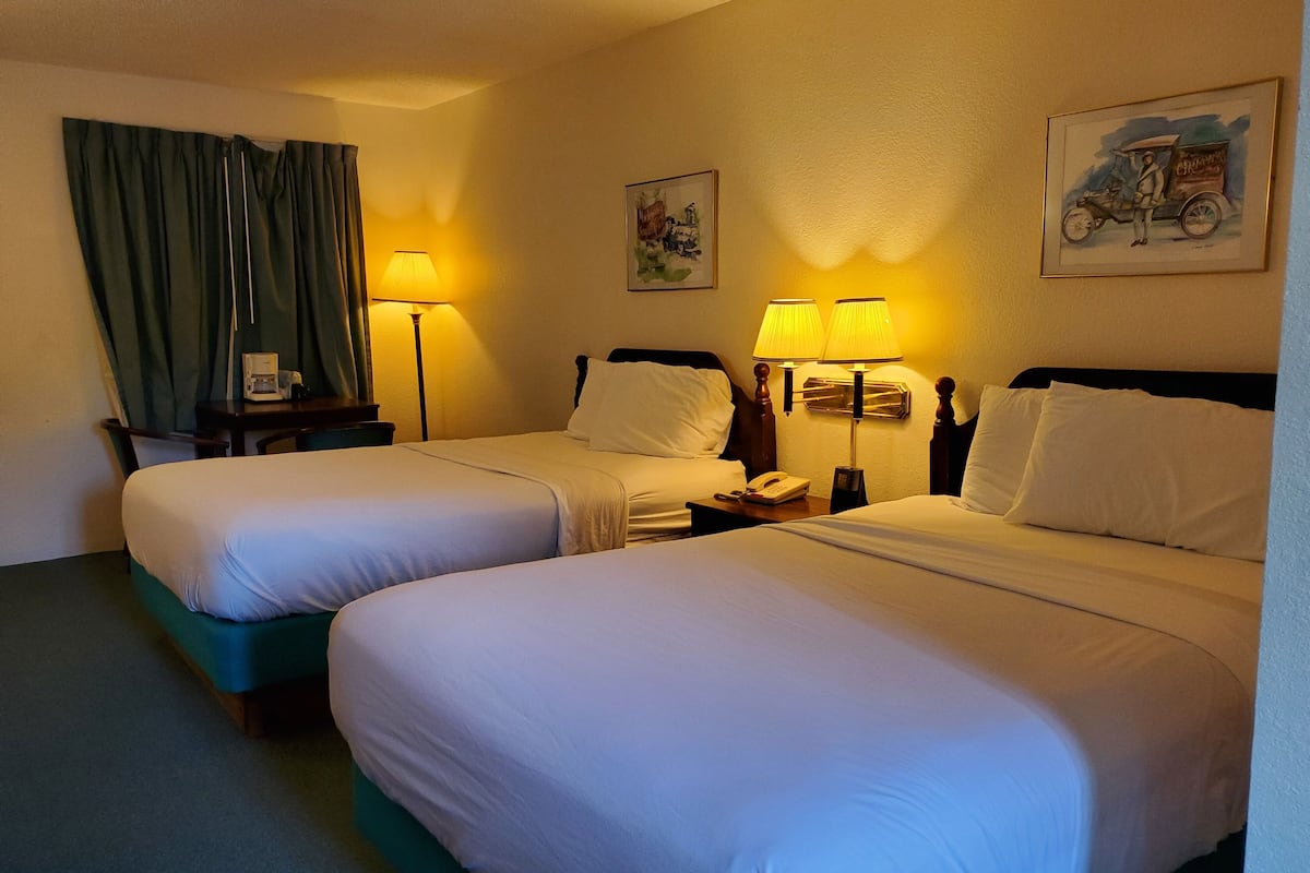 Ett hotellrum med två sängar, ett skrivbord med en lampa, en telefon och två tavlor på väggen.