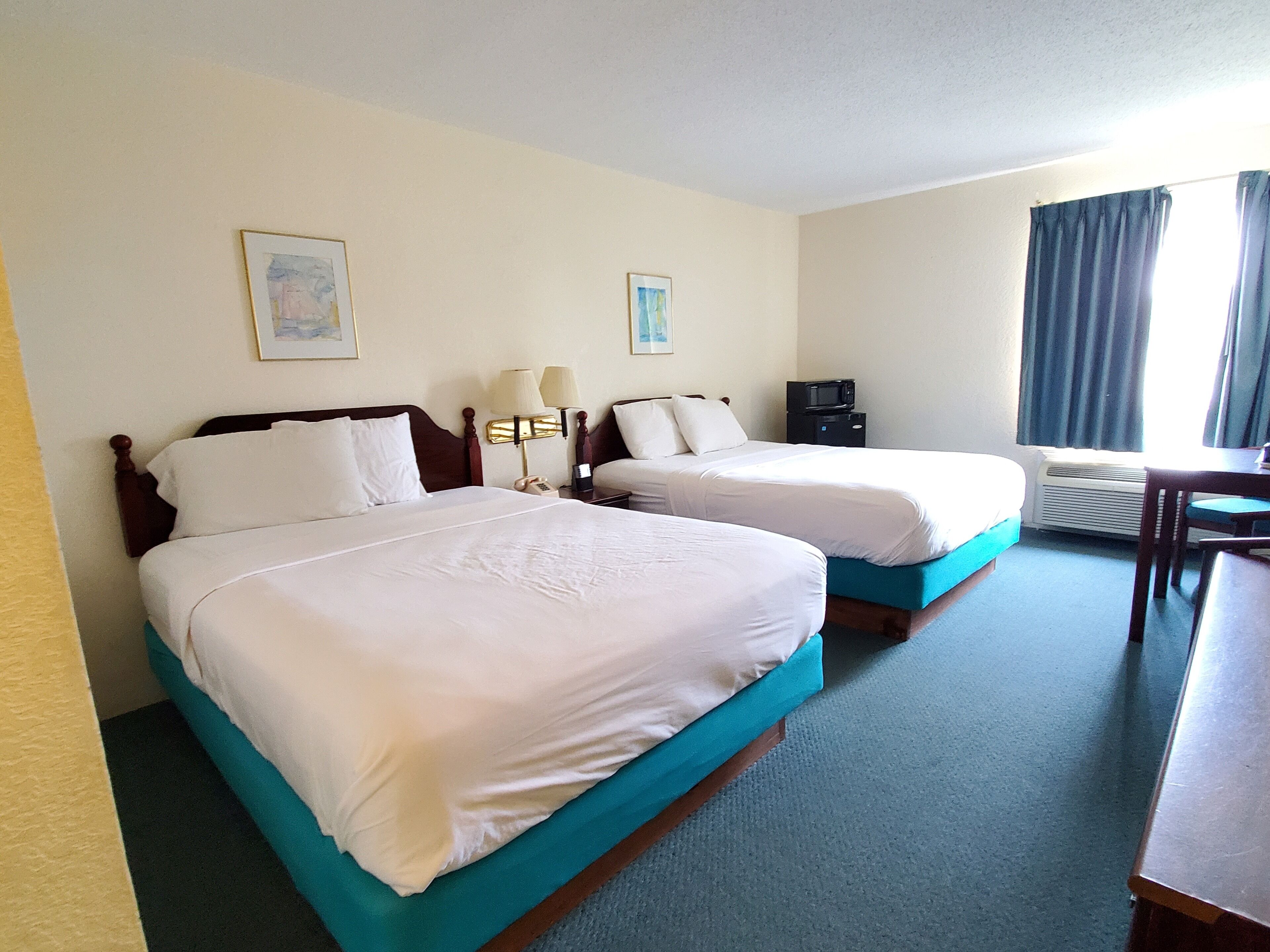 Een hotelkamer met twee bedden, een bureau, een stoel, een magnetron en een raam met gordijnen.