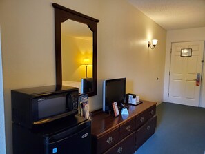 A hotel room with a desk, a television, a mirror, a lamp, and a door. - Up North Hotel (formerly Voyager Inn) (St Ignace)